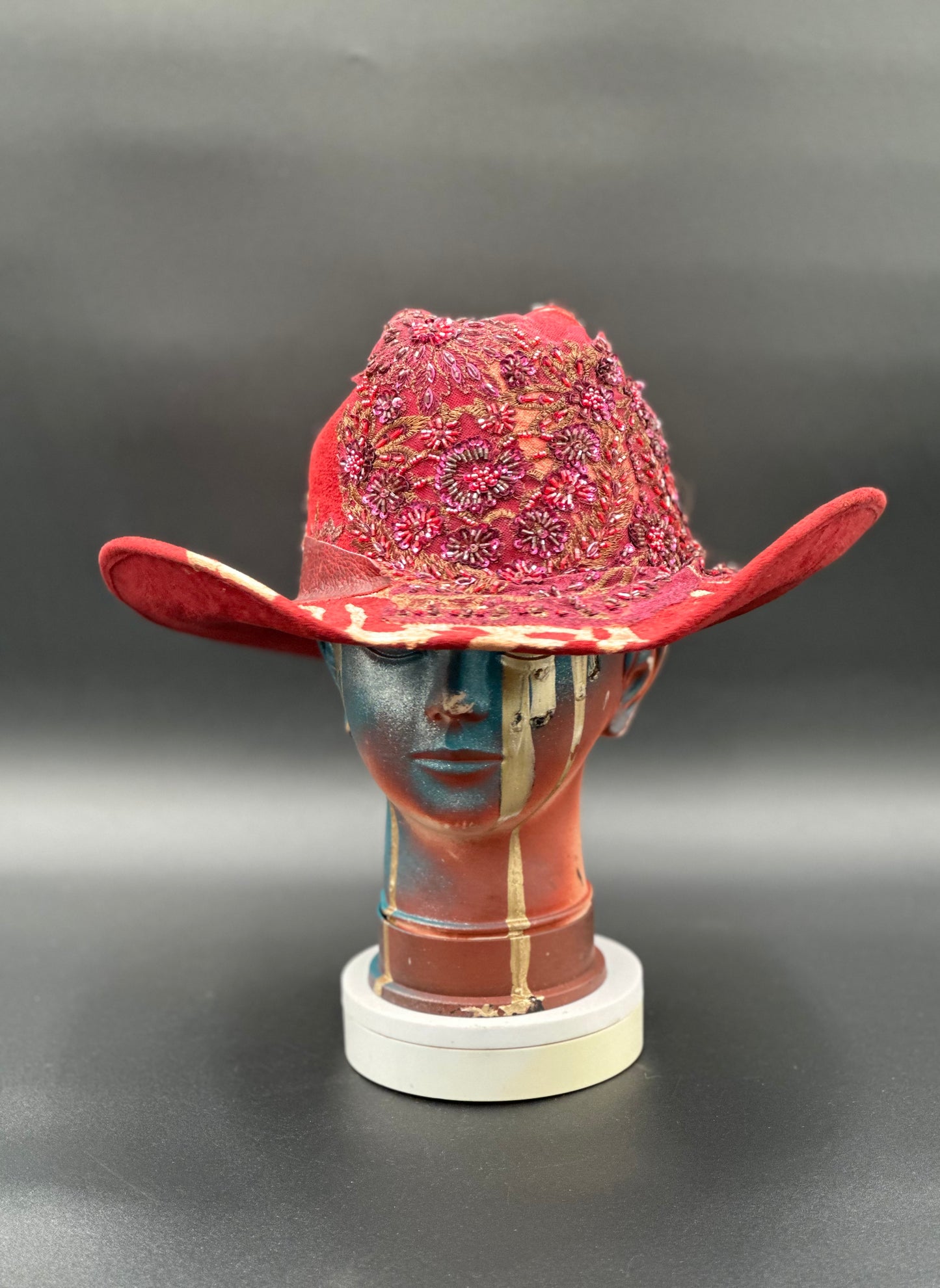 North Miami Red Suede Hat with a hand-painted gold splash and a crystal centerpiece displayed on a mannequin head. Front view showing the hat's full design and shape.