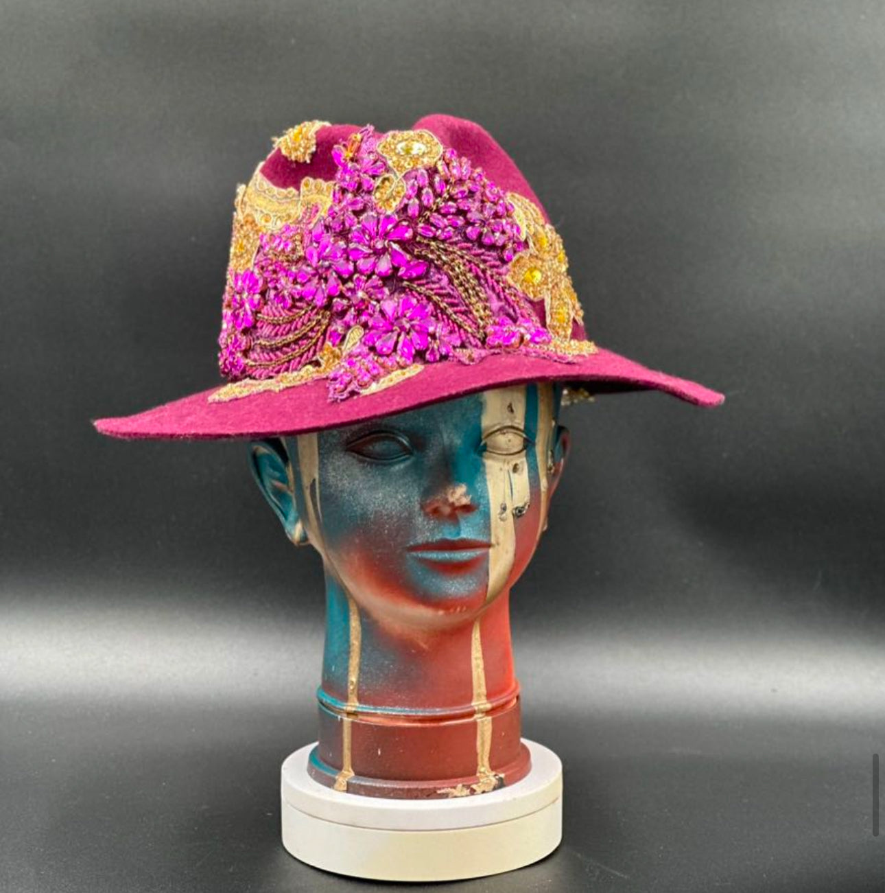 O'porto Magenta Wool Fedora Hat with a crystal ornament centerpiece and gold accents displayed on a mannequin head. Front view showing the hat's full design and shape.