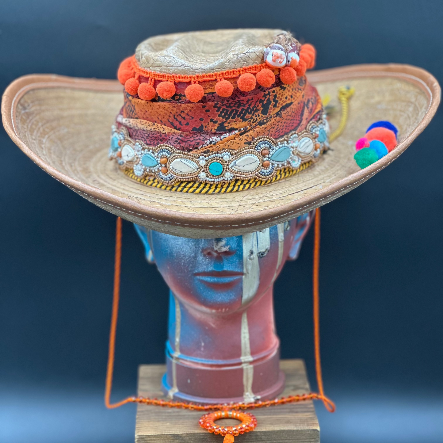Colombia Straw Hat with colorful embellishments, including orange pom-poms, beads, and a bird design, on a mannequin head. Front view showing the full brim and crown.