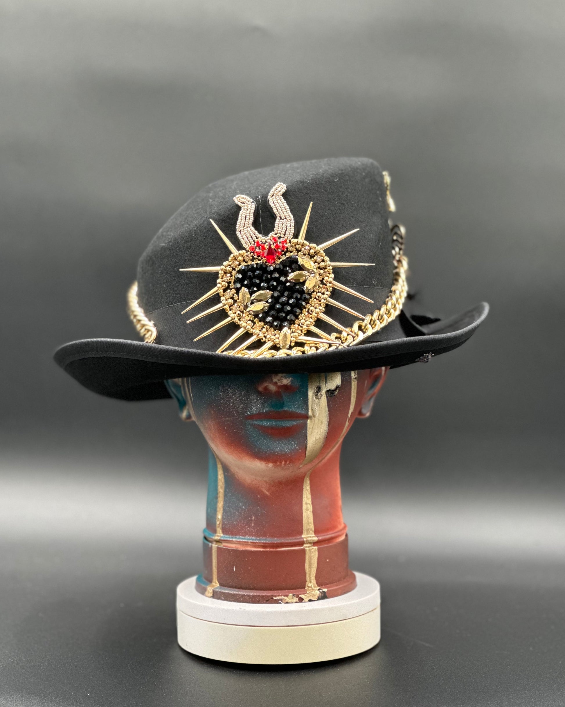 Berlin Black Wool Top Hat with gold chains, spikes, and a central heart design with beadwork. Front view showing the hat's overall shape and style.
