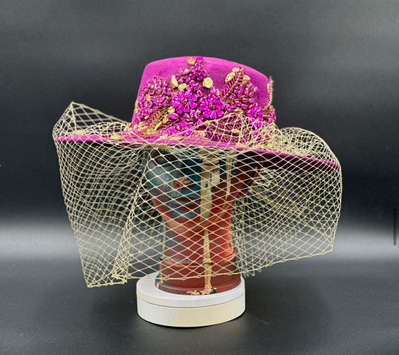 France Magenta Cordobés Wool Hat with a gold veil and crystal centerpiece displayed on a mannequin head. Front view showing the hat's full design and shape.