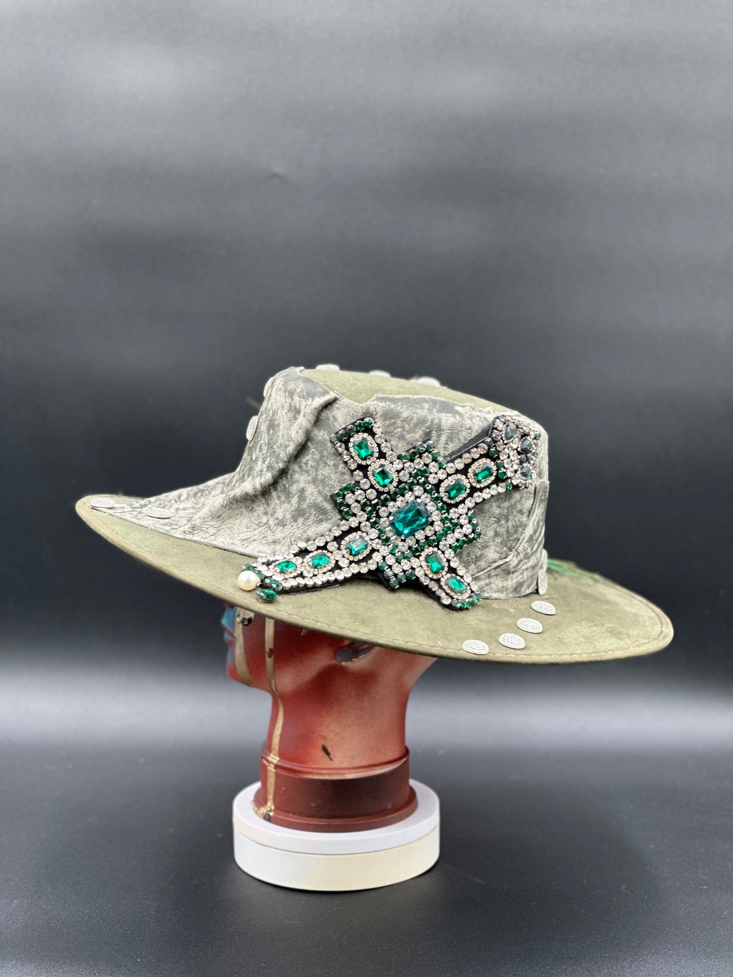 Angled view of the Valencia Green Cordobés Hat, displaying the texture of the fabric and the placement of the crystal cross and feathers.