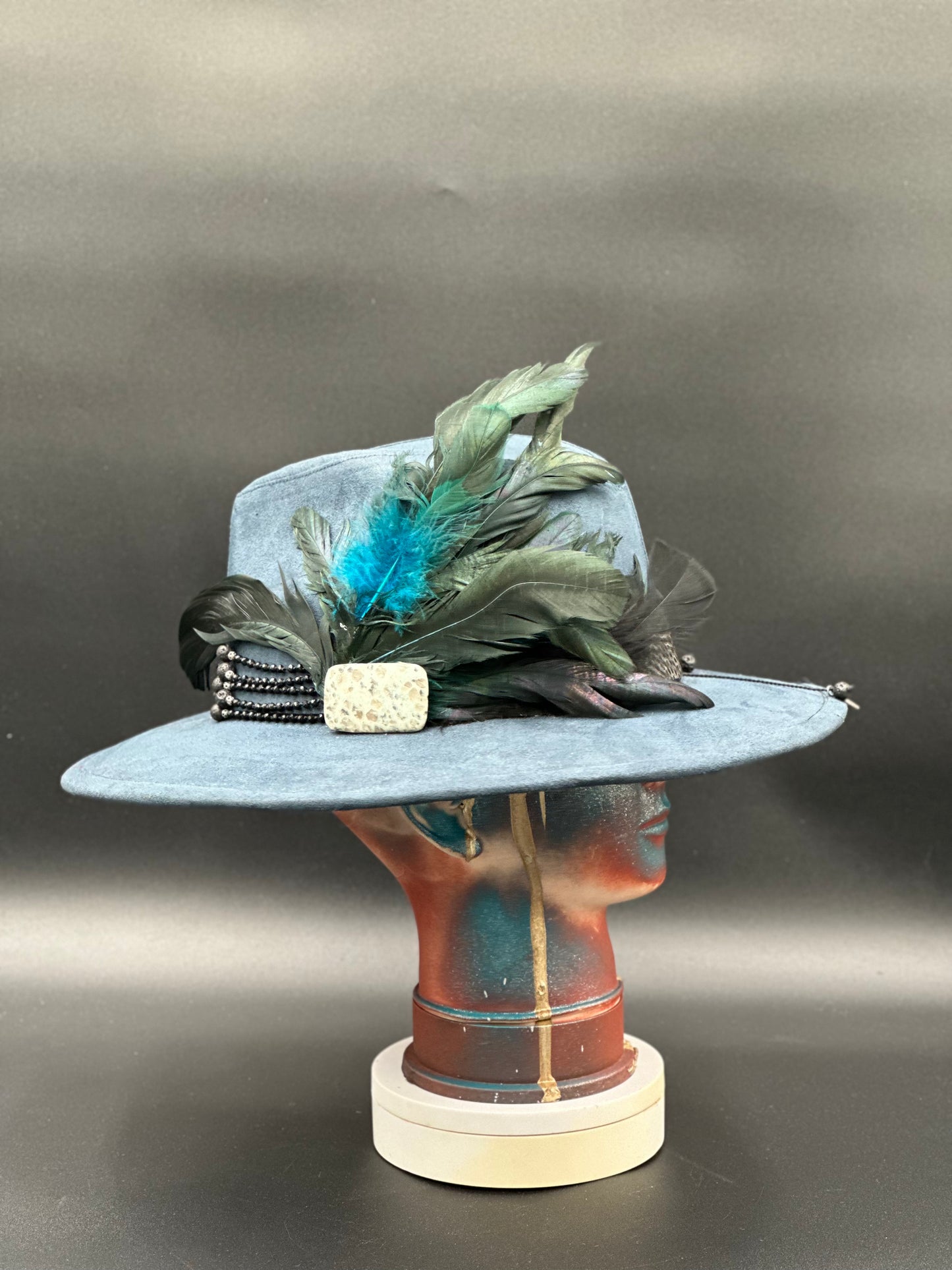 Side view of the Lisboa Blue Suede Fedora Hat on a mannequin head, highlighting the stone placement and the hat's silhouette.