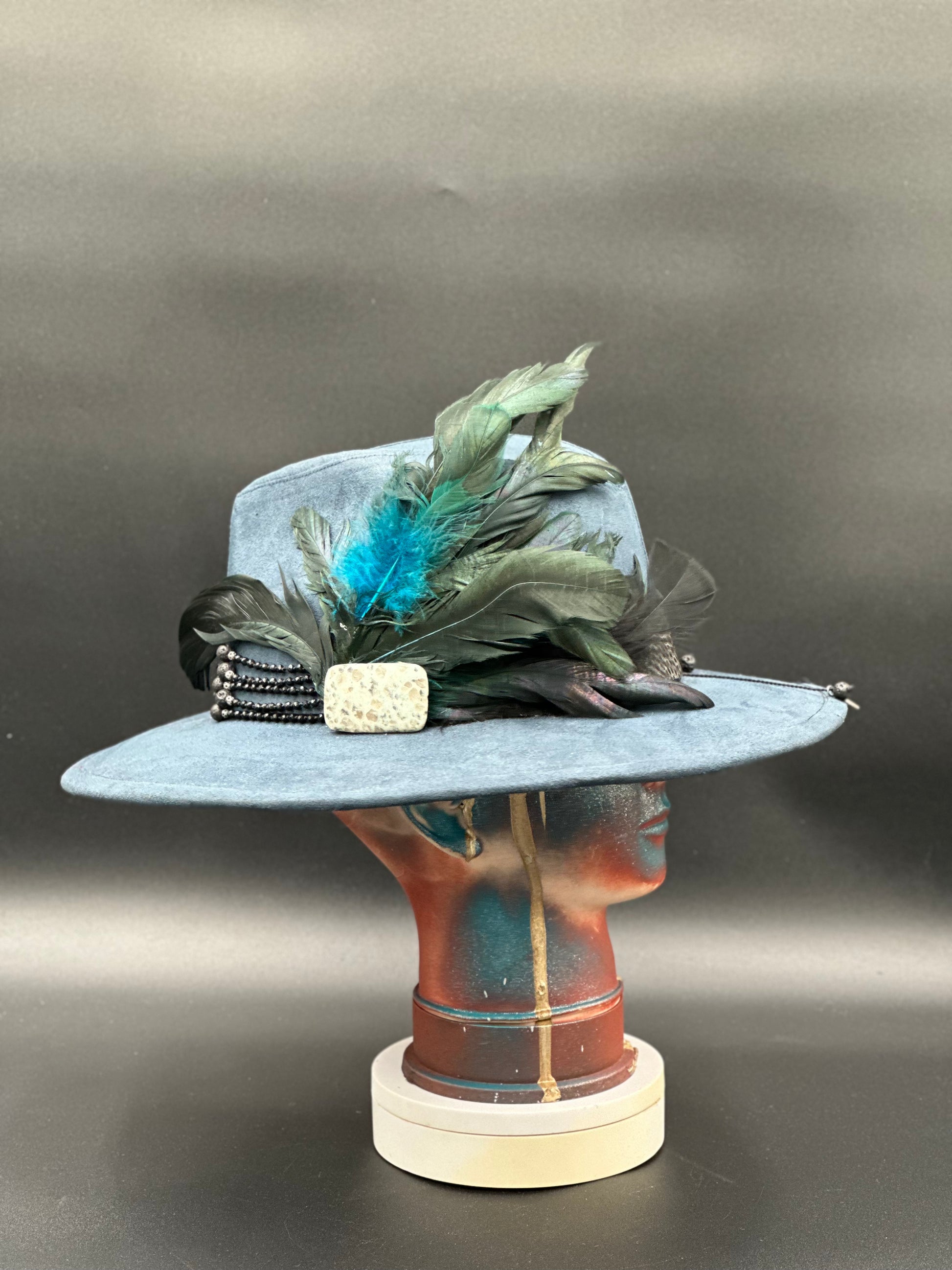 Side view of the Lisboa Blue Suede Fedora Hat on a mannequin head, highlighting the stone placement and the hat's silhouette.