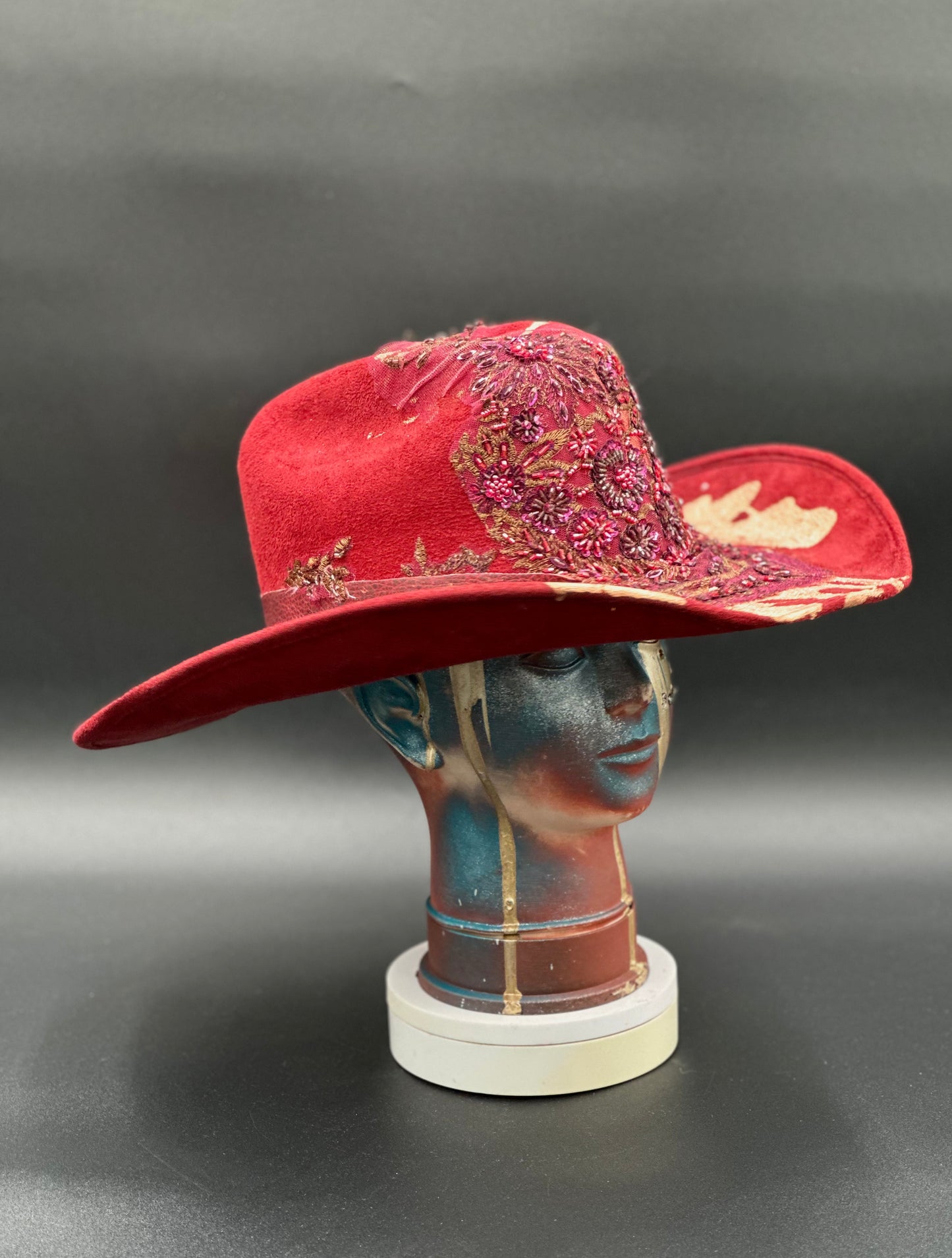 Angled view of the North Miami Red Suede Hat on a mannequin head, displaying the texture of the suede and the placement of the gold splash and crystal.